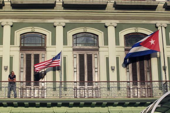 A man stands near the national flags of the U.S. and Cuba (R) on the balcony of a hotel being used by the first U.S. congressional delegation to Cuba since the change of policy announced by U.S. President Barack Obama on December 17, in Havana, January 19, 2015. REUTERS/Stringer