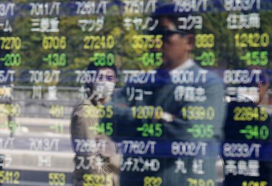Passers-by are reflected on an electronic stock quotation board outside a brokerage in Tokyo, November 17, 2014. REUTERS/Issei Kato